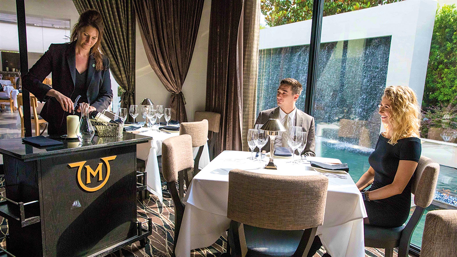 A member of Mastro's staff opening a bottle of wine for two diners sitting at a table